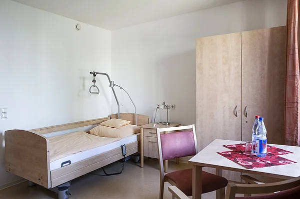 Helles Einzelzimmer des Nellinistrifts mit Pflegebett, Nachttisch, Tisch und Kleiderschrank