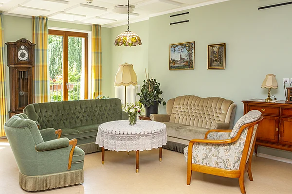 Wohnzimmer des Nellinistifts mit rundem Tisch, Couchs und Sesseln, im Hintergrund eine Standuhr und ein großes Fenster