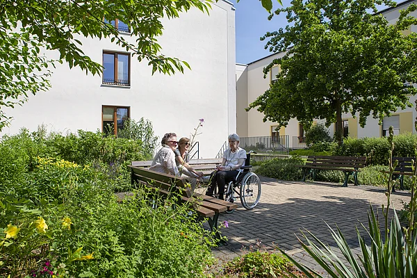 3 Bewohner in der Außenanlage des Nellinistifts sitzend, umgeben von viel Grün 
