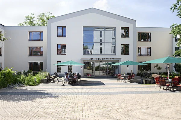 Haupteingang des Nellinistifts mit gepflastertem Vorplatz, Sitzgelegenheiten und Sonnenschirmen
